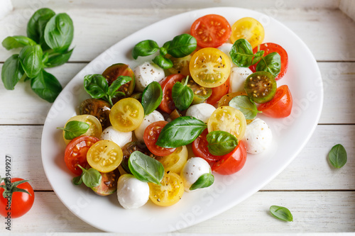 Italian caprese salad with sliced tomatoes, mozzarella cheese, basil, olive oil in wooden bowl. Italian food