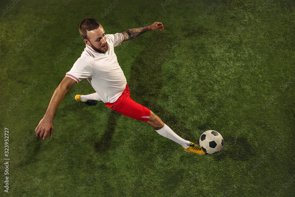 Top view of caucasian football or soccer player on green background of grass. Young male sportive model training, practicing. Kicking ball, attacking, catching. Concept of sport, competition, winning. Top view of caucasian football or soccer player on green background of grass. Young male sportive model training, practicing. Kicking ball, attacking, catching. Concept of sport, competition, winning.