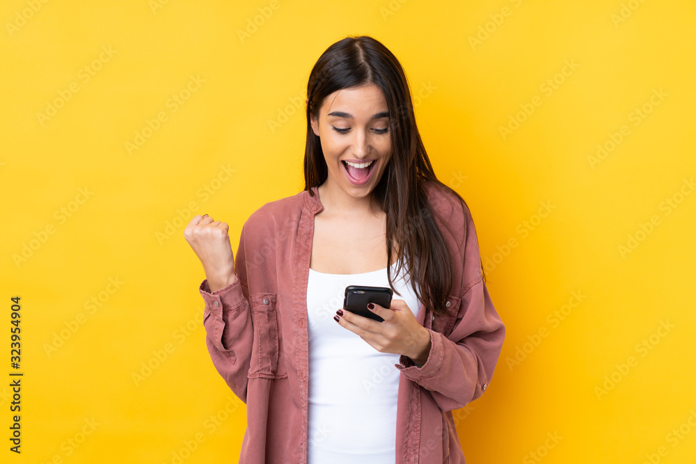 © luismolinero - Young brunette woman over isolated yellow background surprised and sending a message © luismolinero - Young brunette woman over isolated yellow background surprised and sending a message