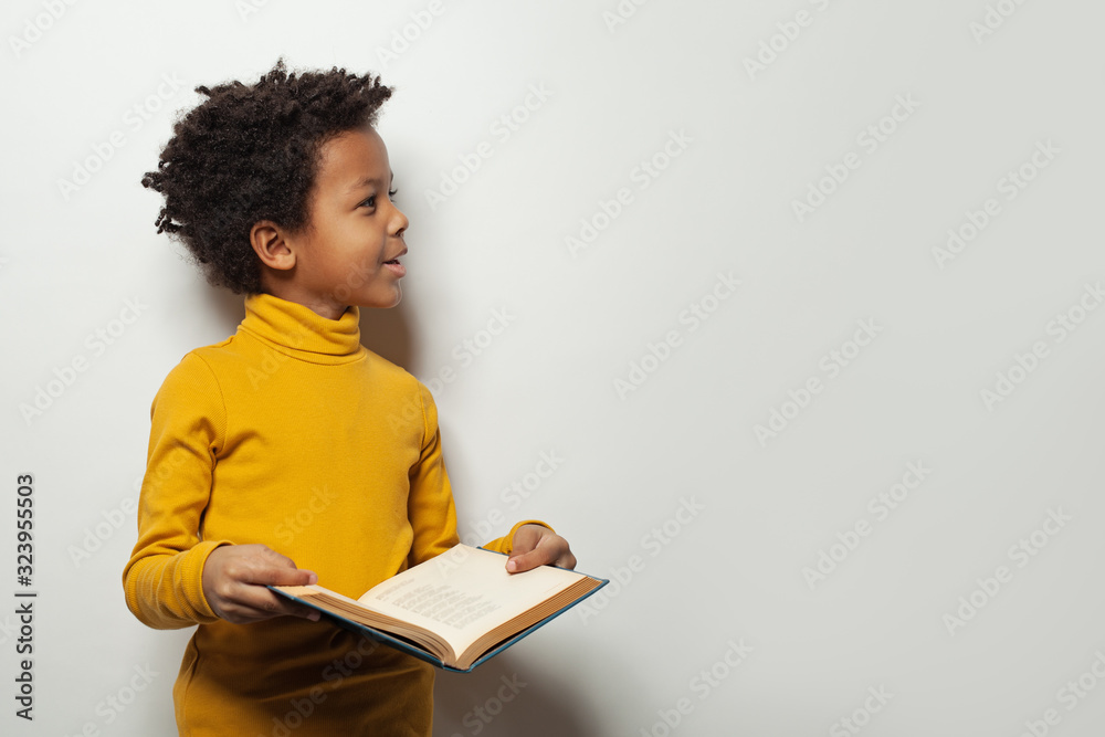 Curious black child boy reading a book on white background - obrazy, fototapety, plakaty 