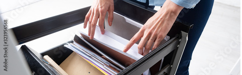 Cropped view of businesswoman searching dossier in paper folders in cabinet driver, panoramic shot photo