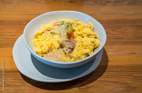 Scrambled eggs with ham and rice in white bowl and white dish on a table.