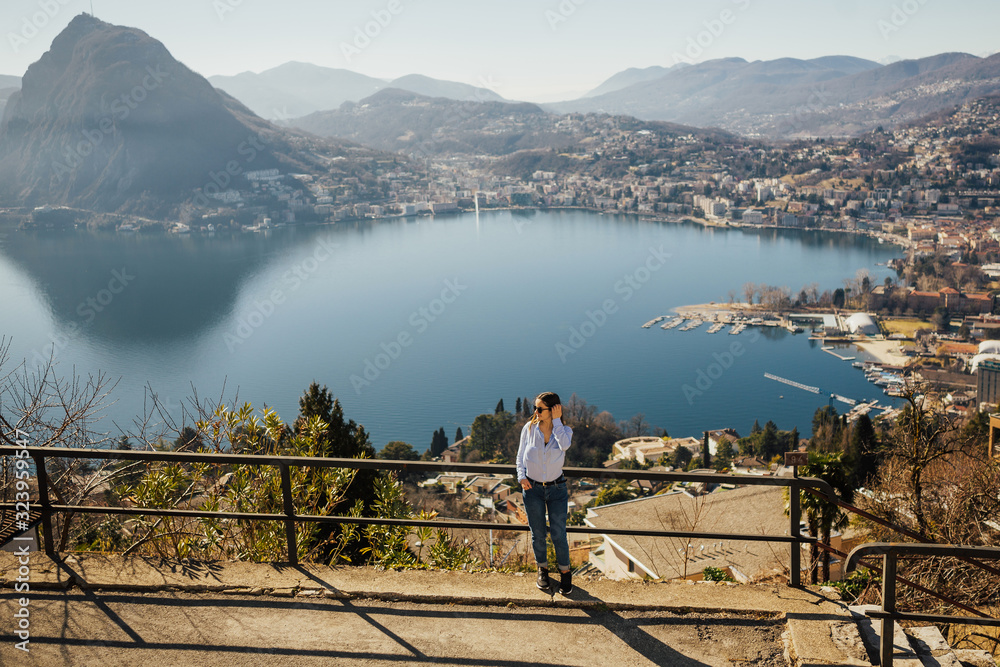 Tourist girl on lake Lugano in Switzerland looking at the panorama. Girl standing top of monte Bre.Tourist spot. View at lake and city. Girl admire the panorama.
