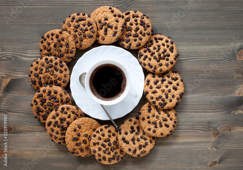 A stack of chocolate chip cookies around coffee cup on a wooden table