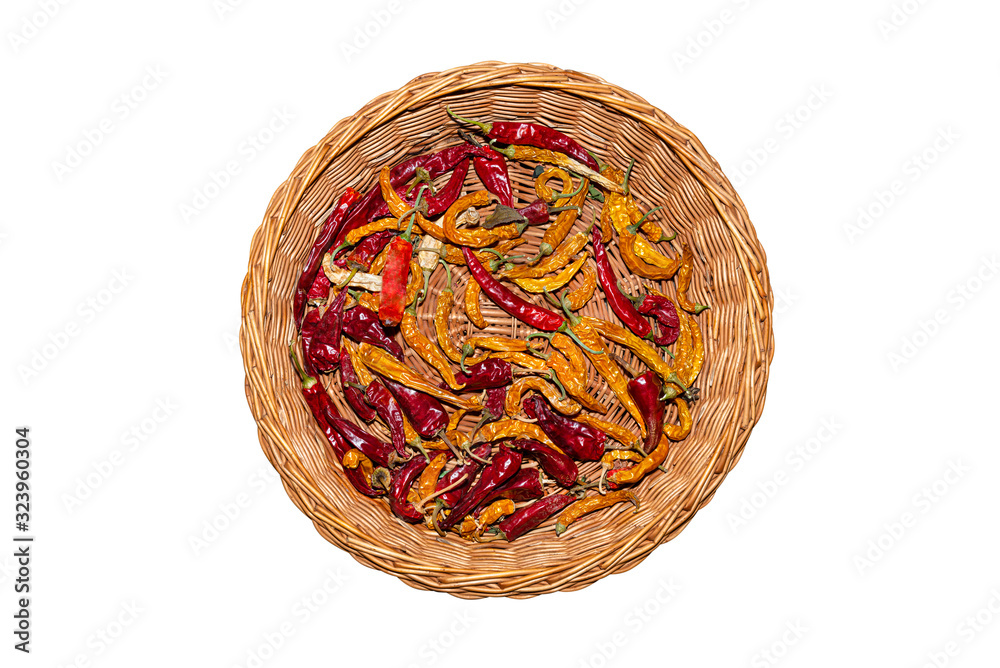 Dried peppers in different colors lying in a round wicker basket, flat top view, isolated on a white background with a clipping path.