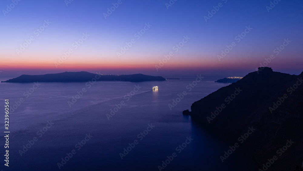 A Cruise ship sailing out of the bay at Santorini, just after sunset and during blue hour.