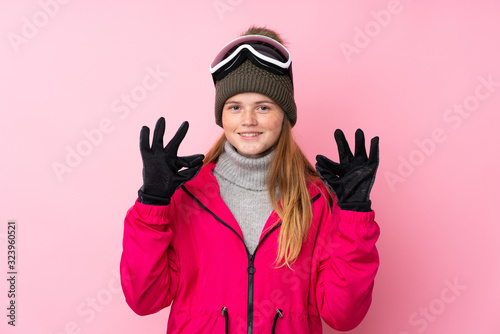 Ukrainian teenager skier girl with snowboarding glasses over isolated pink background showing an ok sign with fingers