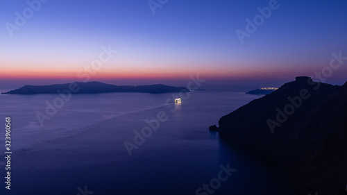 A Cruise ship sailing out of the bay at Santorini, just after sunset and during blue hour.