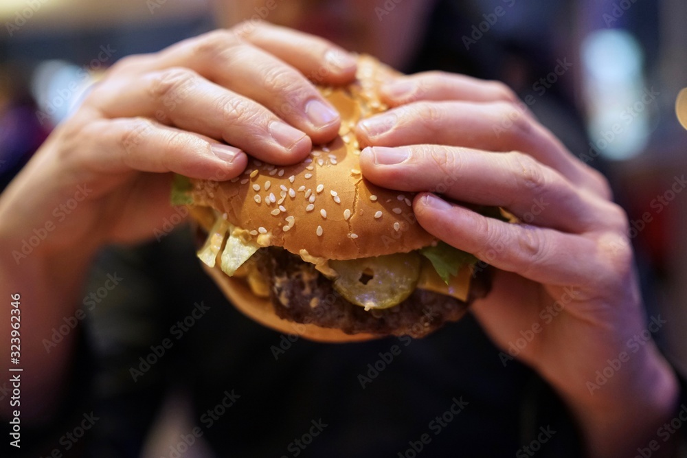 Close-up of man holding eating fastfood cheeseburger Close-up of man holding eating fastfood cheeseburger