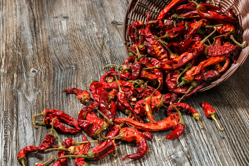 dried red hot chilli peppers strews from a basket on old wooden table