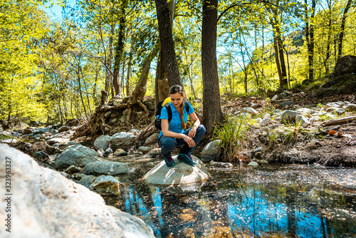Photography Hiking woman sitting on a stone in the middle of a creek passing the woods