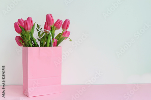 A bouquet of pink tulips in a pink paper bag, space for text