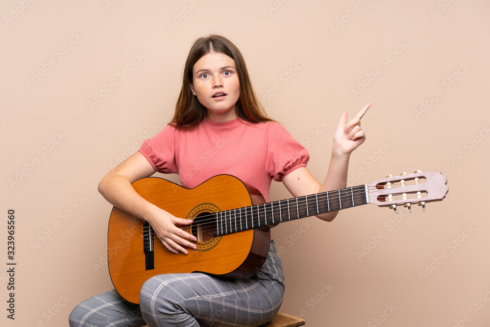 Ukrainian teenager girl with guitar over isolated background surprised and pointing finger to the side Ukrainian teenager girl with guitar over isolated background surprised and pointing finger to the side