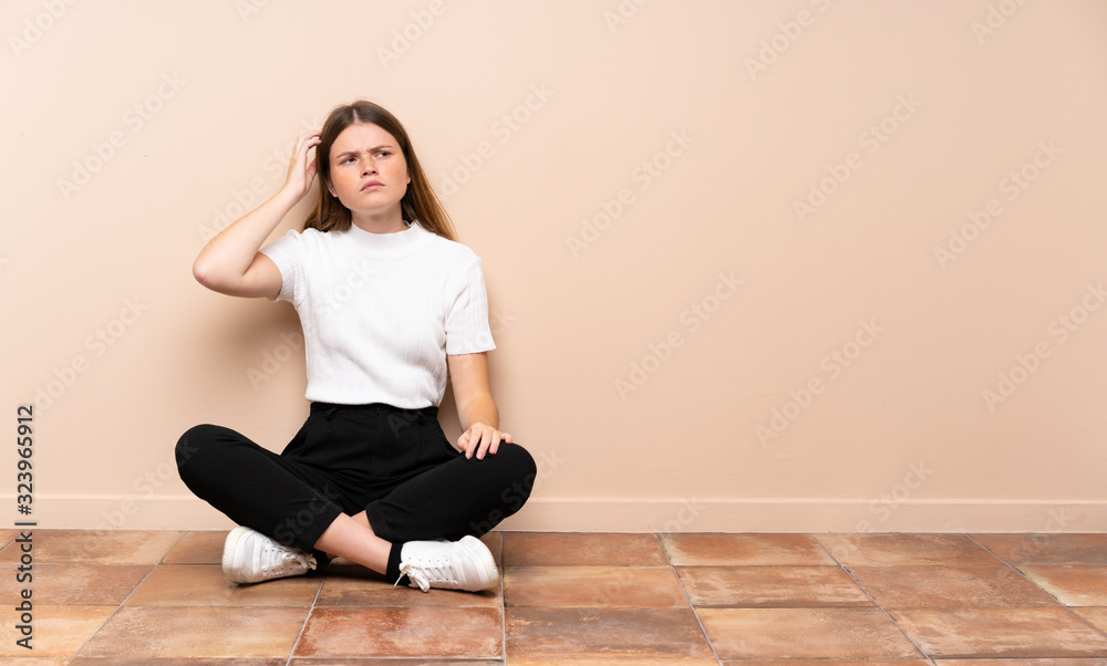 Ukrainian teenager girl sitting on the floor having doubts while scratching head Ukrainian teenager girl sitting on the floor having doubts while scratching head