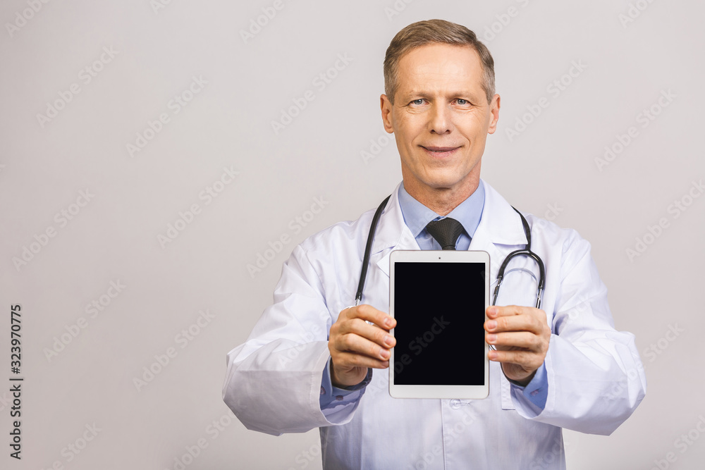 Portrait of senior happy doctor showing tablet computer blank screen isolated over grey background. Portrait of senior happy doctor showing tablet computer blank screen isolated over grey background.