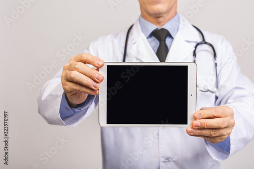 Portrait of senior happy doctor showing tablet computer blank screen isolated over grey background.