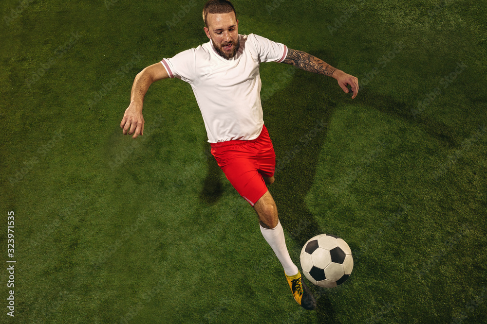 Top view of caucasian football or soccer player on green background of grass. Young male sportive model training, practicing. Kicking ball, attacking, catching. Concept of sport, competition, winning. Top view of caucasian football or soccer player on green background of grass. Young male sportive model training, practicing. Kicking ball, attacking, catching. Concept of sport, competition, winning.