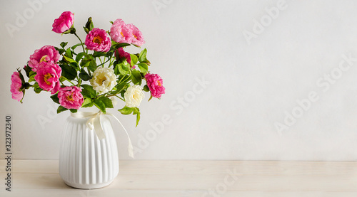 Holiday card background for an inscription. Twigs of a blooming rosehip in a white vase on a white background with copy space. March 8 Women's Day, Mother's Day