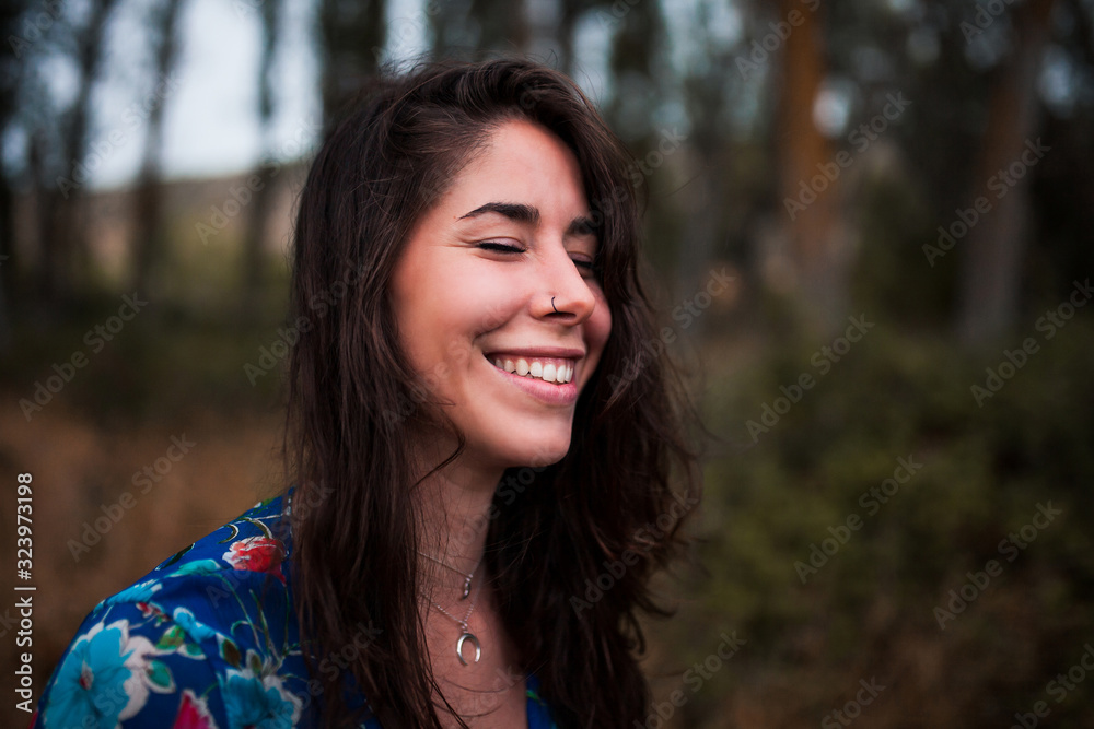 Young smiling woman wearing dress in the forest with closed eyes