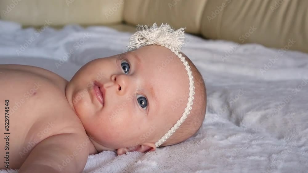 Child look at the camera close-up shot. Cute little baby looking at the camera. The child looks around and then smiles. Cute newborn baby with a beautiful bow.. The concept of child care, parental Child look at the camera close-up shot. Cute little baby looking at the camera. The child looks around and then smiles. Cute newborn baby with a beautiful bow.. The concept of child care, parental