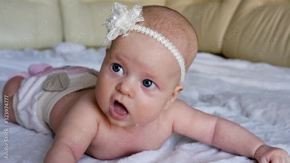 Child look at the camera close-up shot. Cute little baby looking at the camera. The child looks around and then smiles. Cute newborn baby with a beautiful bow.. The concept of child care, parental Child look at the camera close-up shot. Cute little baby looking at the camera. The child looks around and then smiles. Cute newborn baby with a beautiful bow.. The concept of child care, parental