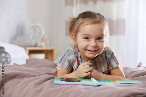 Cute little girl with book on bed at home