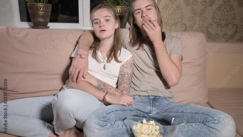Young cute couple sitting hugging in living room, watching TV, eating popcorn. Young cute couple sitting hugging in living room, watching TV, eating popcorn.
