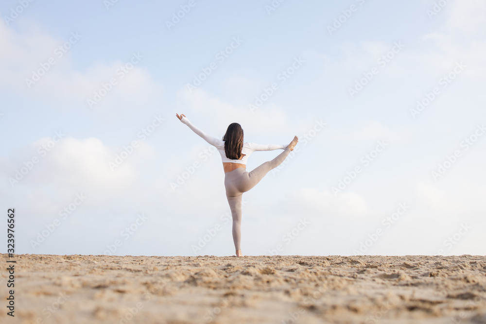 Fit girl doing yoga in the beach by the sea on a sunny day