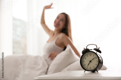 Young woman stretching at home in morning, focus on alarm clock