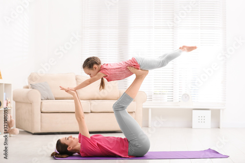 Young mother with little daughter practicing yoga at home