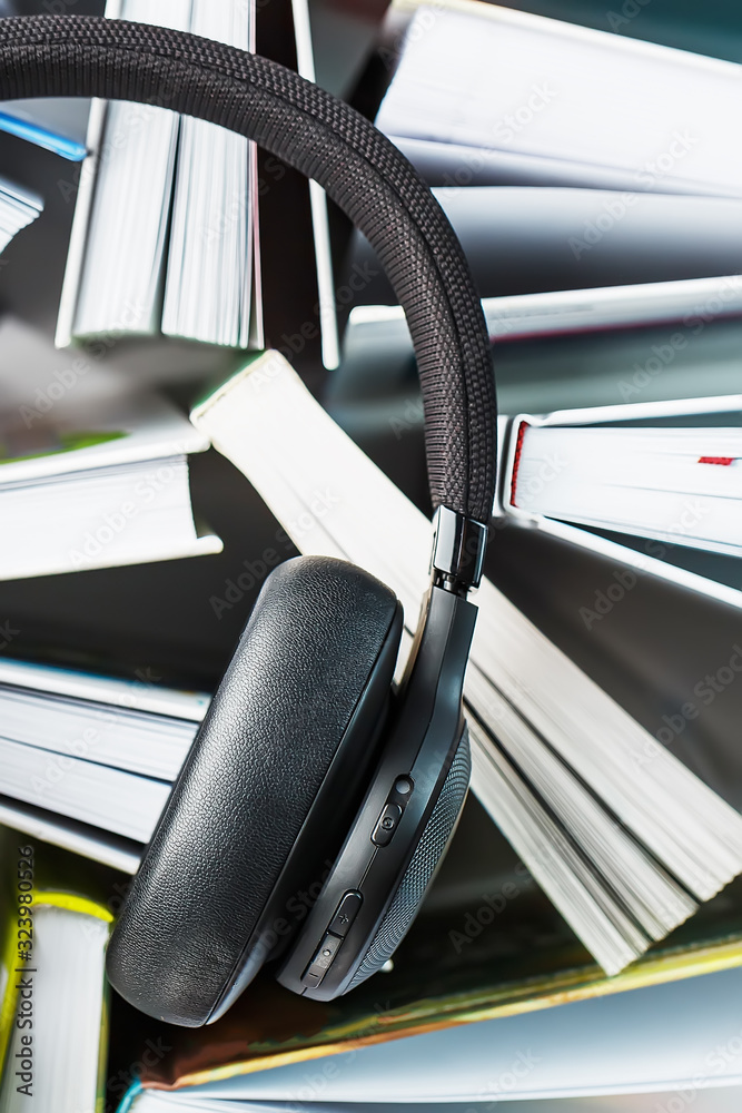 Wireless overhead black headphones lie on the books. The concept of learning through an audiobook. To listen to the book. Wireless overhead black headphones lie on the books. The concept of learning through an audiobook. To listen to the book.