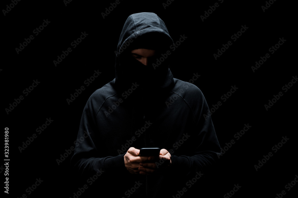 hacker in hood and mask using smartphone isolated on black hacker in hood and mask using smartphone isolated on black