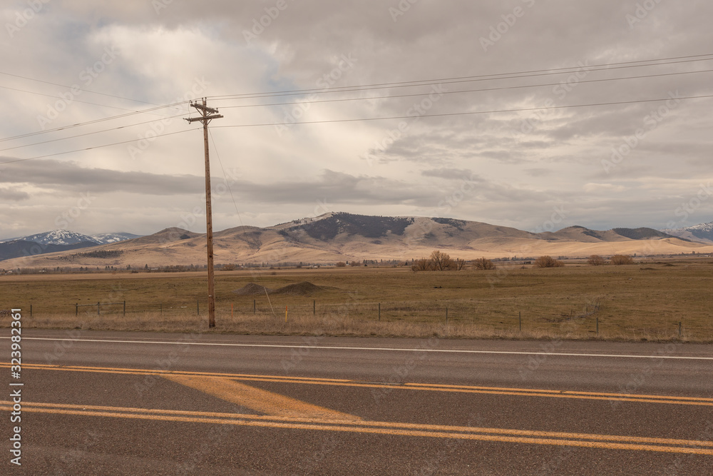 Telephone pole next to empty highway with rolling hills and mountains in distance