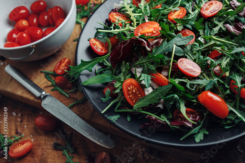 Close-up rocket salad with tomato on black plate with nife and white bowl  photo