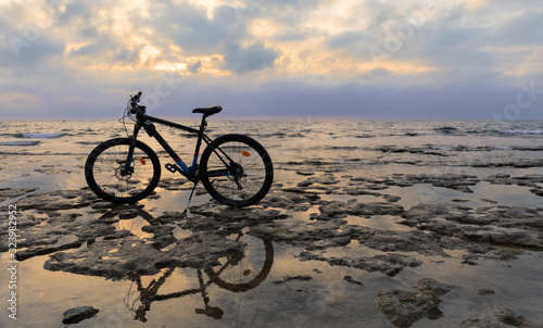 A biker has parked his mountain bike on the rocky coast near the Spanish port city of Torrevieja. It's morning after sunrise. A beautiful cloudy sky in the background. © wewi-creative