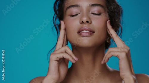 beautiful girl moisturizing and massaging face smiling to camera isolated on blue