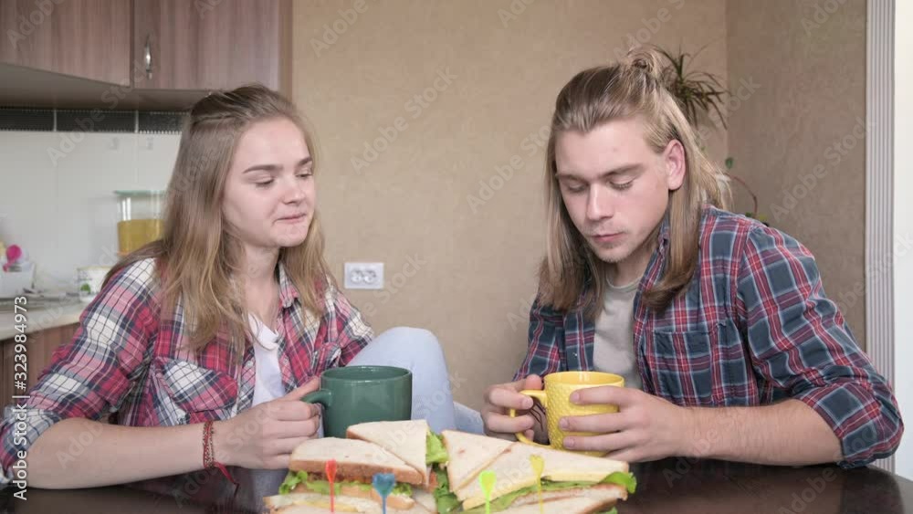 Young couple sitting in kitchen, drinking from cups, chatting. Closeup Young couple sitting in kitchen, drinking from cups, chatting. Closeup
