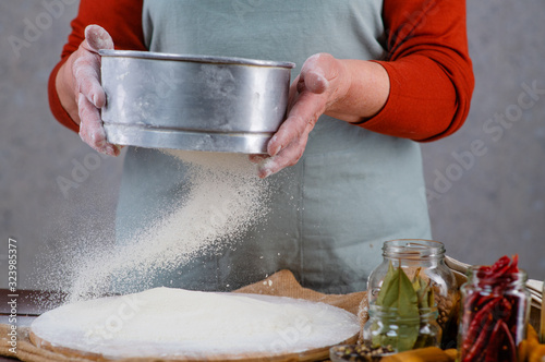 Woman cook sifts the sieve flour on the table. Frozen motion