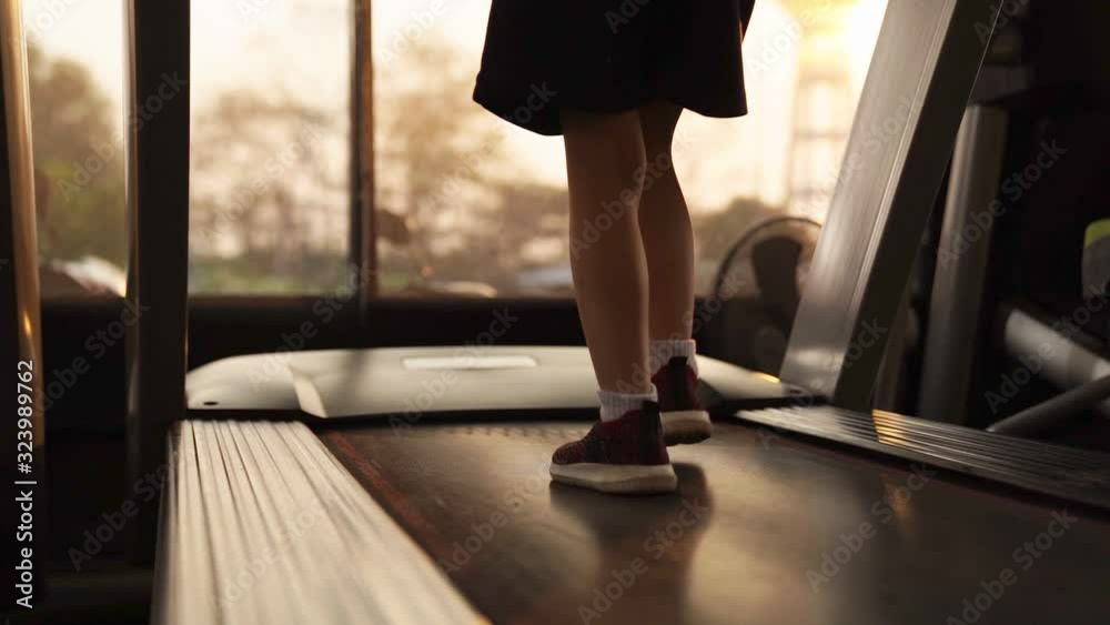 Slow motion footage of supposedly young girl legs in sneakers running on treadmill.