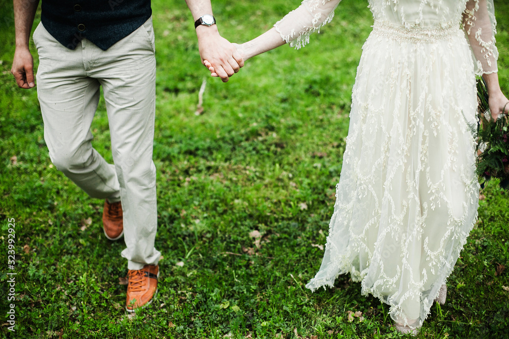 The groom and the bride walk through the woods holding hands. Wedding in the forest. The groom and the bride walk through the woods holding hands. Wedding in the forest.
