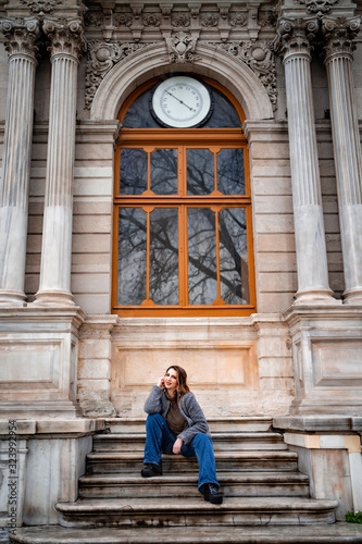 Red haired beautiful girl sitting on the steps of an old building in the rain