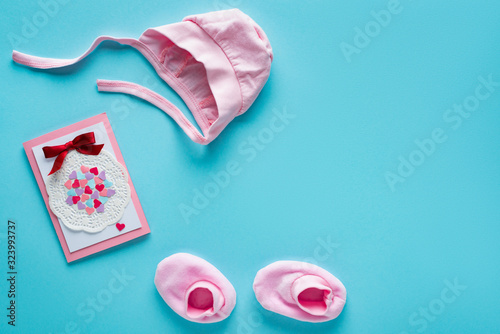 Top view of pink baby clothes and greeting card on blue background, concept of mothers day