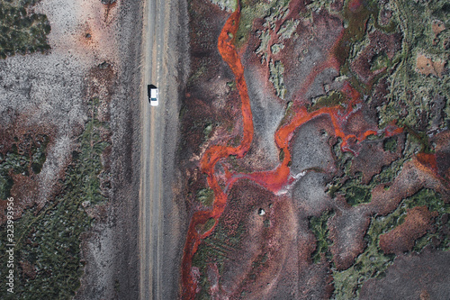 Naklejka Off road car driving next to the beautiful textured red river. Aerial view of a interesting patterns in Iceland.