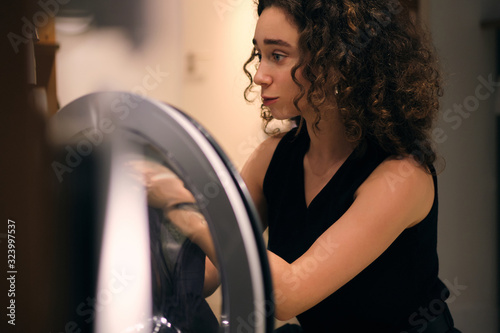 Canvas Print Portrait of brunette girl taking out clothes from washing machine in modern self