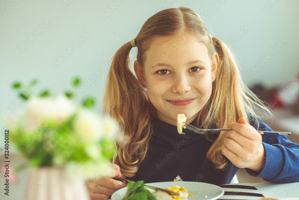Cute blonde teen girl eating eggs benedict with knife and fork foto de