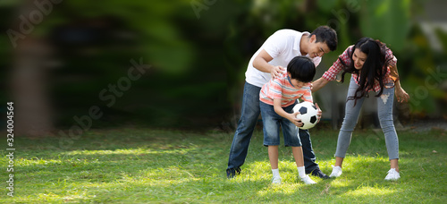 Family playing football or soccer in green garden together their leisure time at summer holiday