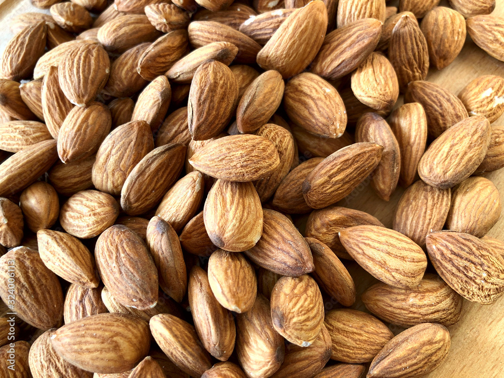 Fototapeta premium Food background. Many peeled almonds on a wooden background. Texture of almond kernels. Background of brown nuts. Close-up, horizontal, cropped shot. Concept of vegetarianism and healthy eating.