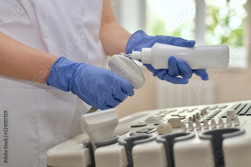  Hands with gloves starts squeezing out a little bit a transparent gel to the ultrasound scanner's sensor.