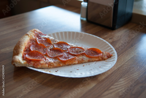 Slice of fresh new york style pepperoni pizza on a paper plate