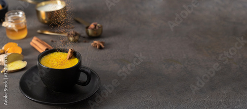 Принти на полотні Cinnamon pouring on dark mug with Golden milk beverage on concrete background